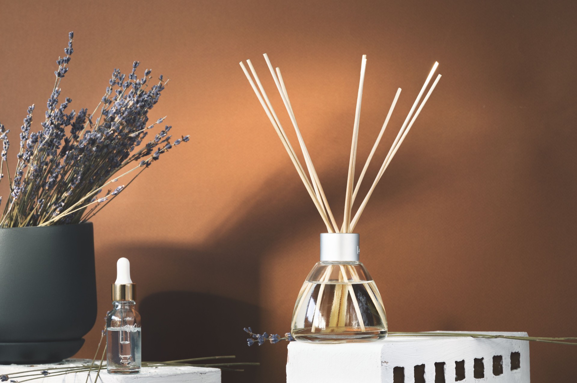 Air fragrance with lavender aroma. Glass bottle container with wood stick diffusers and essential oils. Dry lavender in a dark pot on a brown background.